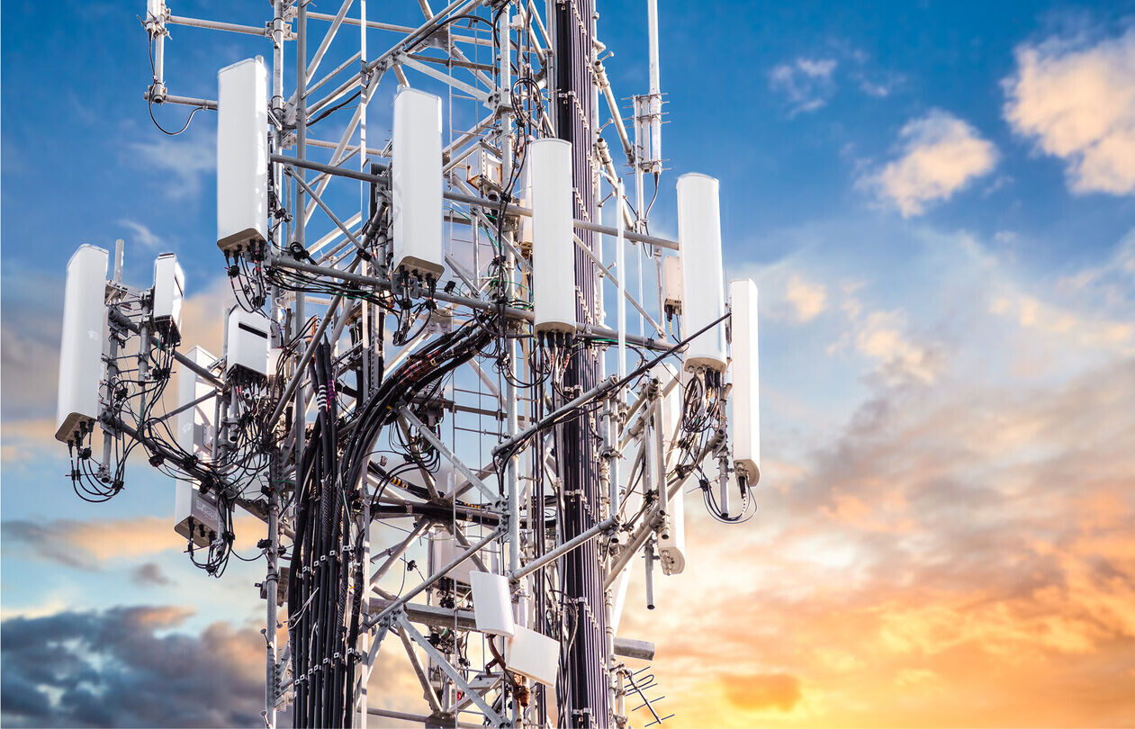 A close-up of a telecommunications tower with multiple antennas against a colorful sunset sky.