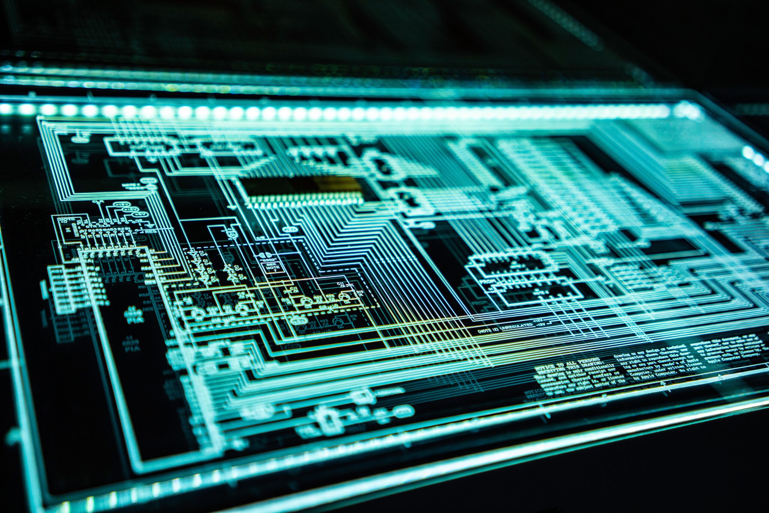 A close-up of a circuit board with intricate lines and patterns illuminated in blue and green tones.