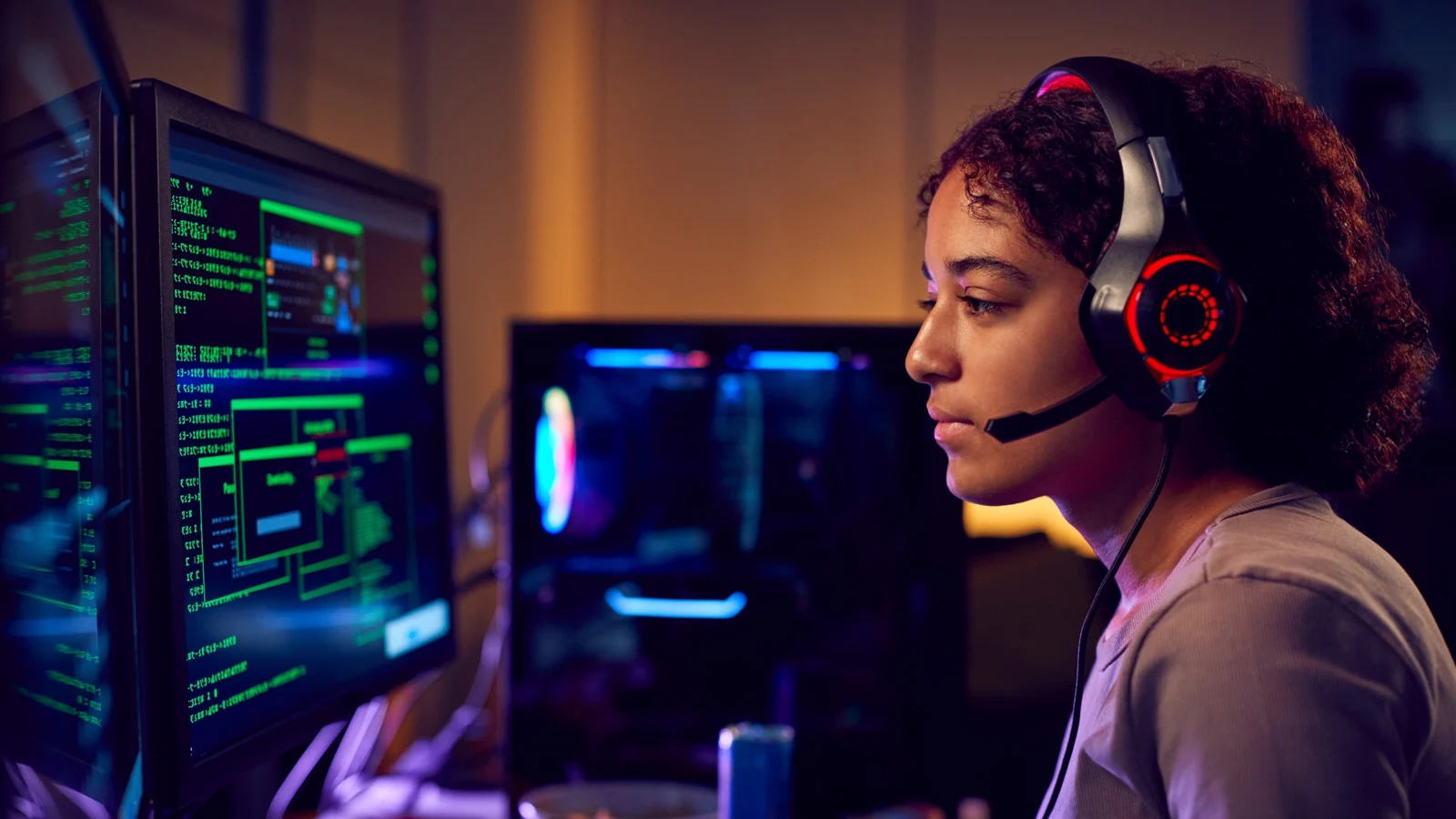 A focused individual wearing a headset sits in front of multiple monitors displaying green code and digital interfaces.