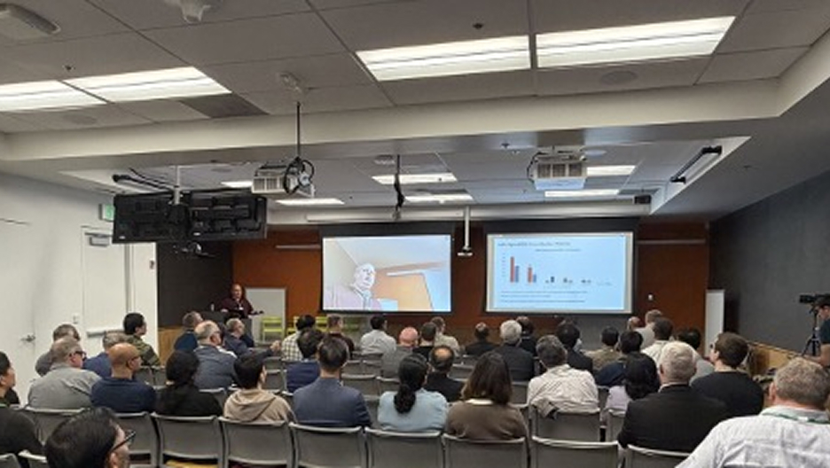 会议室里坐满了与会者,他们正在观看屏幕上的演示文稿,演示文稿上有图表和演讲者。